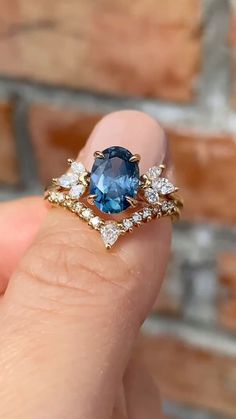 a woman's hand holding an engagement ring with a blue stone surrounded by diamonds