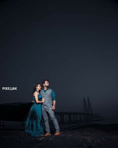 a man and woman standing next to each other in front of the ocean at night