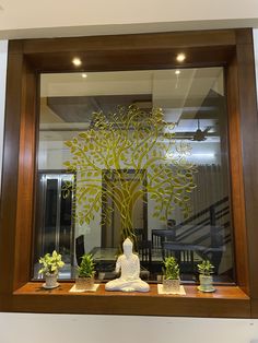 a buddha statue sitting in front of a window with a tree cut out on it