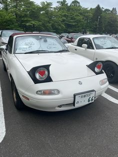 two white sports cars parked next to each other in a parking lot with trees in the background