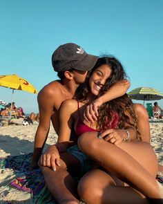 two people are sitting on the beach and one person is hugging his girlfriend's chest