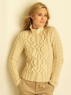 a woman standing in front of a white wall wearing a sweater and tan pants with her hands on her hips