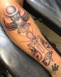 a tattoo with an egyptian cross and symbols on the arm that is sitting on a person's leg