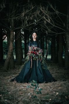 a woman in black dress standing in the woods with flowers on her head and face