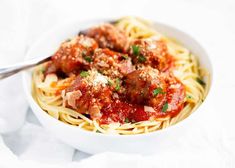 a white bowl filled with spaghetti and meatballs on top of a table next to a fork