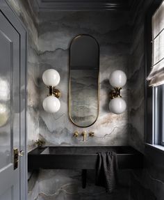 a bathroom with marble walls and black counter top, two lights on either side of the sink