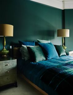 a bedroom with green walls and blue bedspread, two lamps on either side of the bed