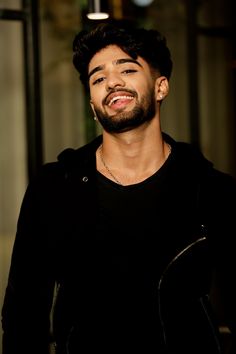 a man with a beard smiling and wearing a black shirt in front of a building