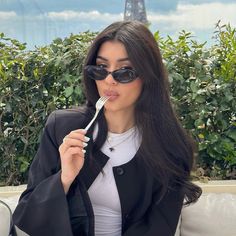 a woman in sunglasses is brushing her teeth with an electric toothbrush while sitting on a bench near the eiffel tower