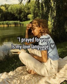 a woman sitting on top of a blanket next to a river with the words i pray for