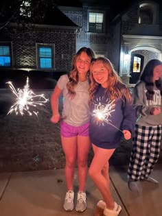 two girls are posing with sparklers in front of a house at night, while another girl is standing next to her