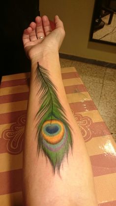 a peacock feather tattoo on the arm of a woman's left arm and wrist