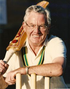 an older man with glasses holding a bat and smiling at the camera while sitting in a chair