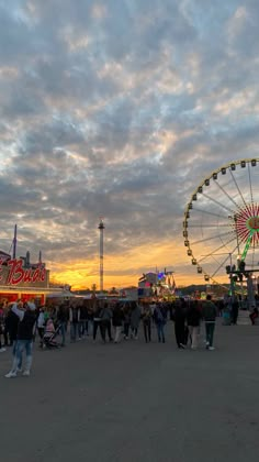 people are standing around in front of a ferris wheel at an amusement park during the sunset