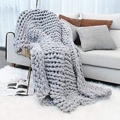 a large chunky knitted blanket sitting on top of a white rug next to a couch