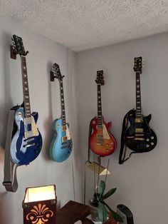 three guitars are hanging on the wall next to a table with a lamp in it