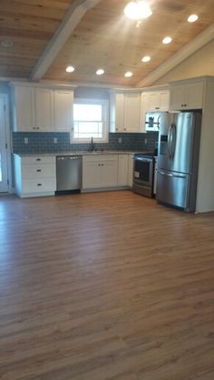 an empty kitchen and living room with wood floors, stainless steel appliances and white cabinets