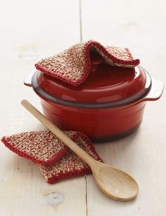 a red casserole dish with two wooden spoons on it and some burlap napkins