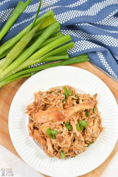 a white plate topped with shredded chicken and green onions on top of a wooden cutting board