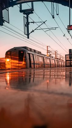 a train traveling down tracks next to power lines and traffic lights at dusk with fog on the ground