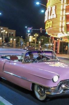 an old pink car parked in front of a theater