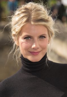 a close up of a woman smiling with her hair in a bun and wearing a turtle neck sweater