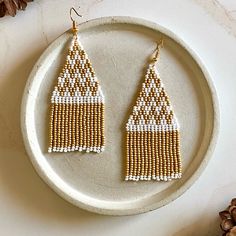 a pair of beaded earrings sitting on top of a white plate next to pine cones