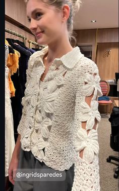 a woman standing in front of a rack of clothes wearing a crochet top