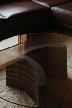 a glass table sitting on top of a white rug next to a brown leather couch