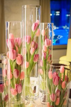 pink tulips in clear vases sitting on a table with other glass vases