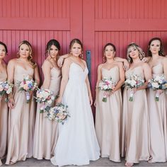 a group of women standing next to each other in front of a red wall holding bouquets