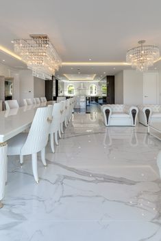 an elegant dining room with white chairs and chandelier hanging from the ceiling, along with marble flooring