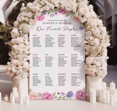 a wedding seating chart with flowers and candles on the table in front of an arch