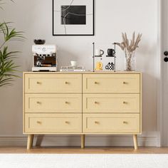 a room with a dresser, potted plant and pictures on the wall above it