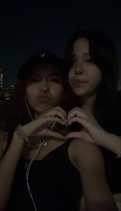 two young women standing next to each other in front of a city skyline at night