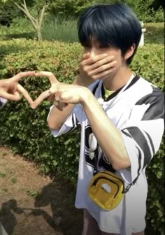 a boy making a heart with his hands while standing in front of bushes and trees