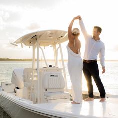 a man and woman standing on the back of a boat in the water, holding hands