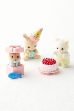 three small toy animals sitting next to each other on a white surface with one holding a piece of cake