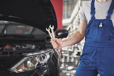 a man in overalls holding wrenches next to a car