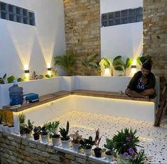 a man sitting on a bench surrounded by potted plants and lights in a room