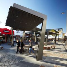 people are walking around an outdoor shopping area with benches and tables on the side walk