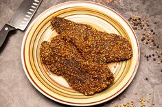 two pieces of meat on a plate next to a knife and seasoning flakes