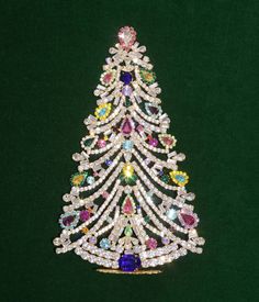 a christmas tree brooch with multicolored stones on it's sides and an elaborate center piece