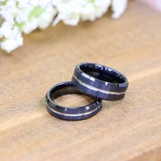 two black rings sitting on top of a wooden table next to white and green flowers