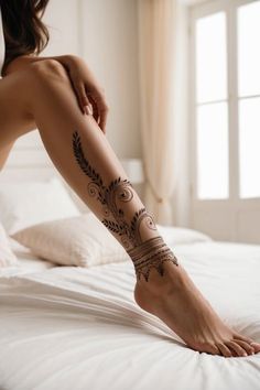 a woman's legs with tattoos on them sitting on top of a white bed