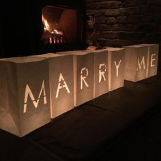 three paper bags with the words marry me on them in front of a fire place