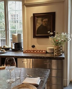 a table with wine glasses and plates on it in front of a window that has a painting above it