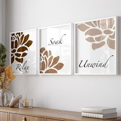 three framed art prints hanging on the wall above a wooden dresser and vase with flowers