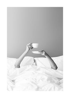 a woman laying in bed with her legs crossed and holding a coffee cup above her head