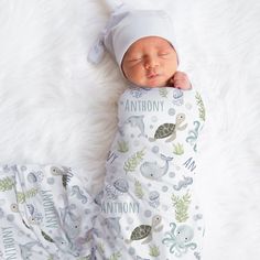 a baby sleeping on top of a white blanket next to a stuffed animal pillow and hat